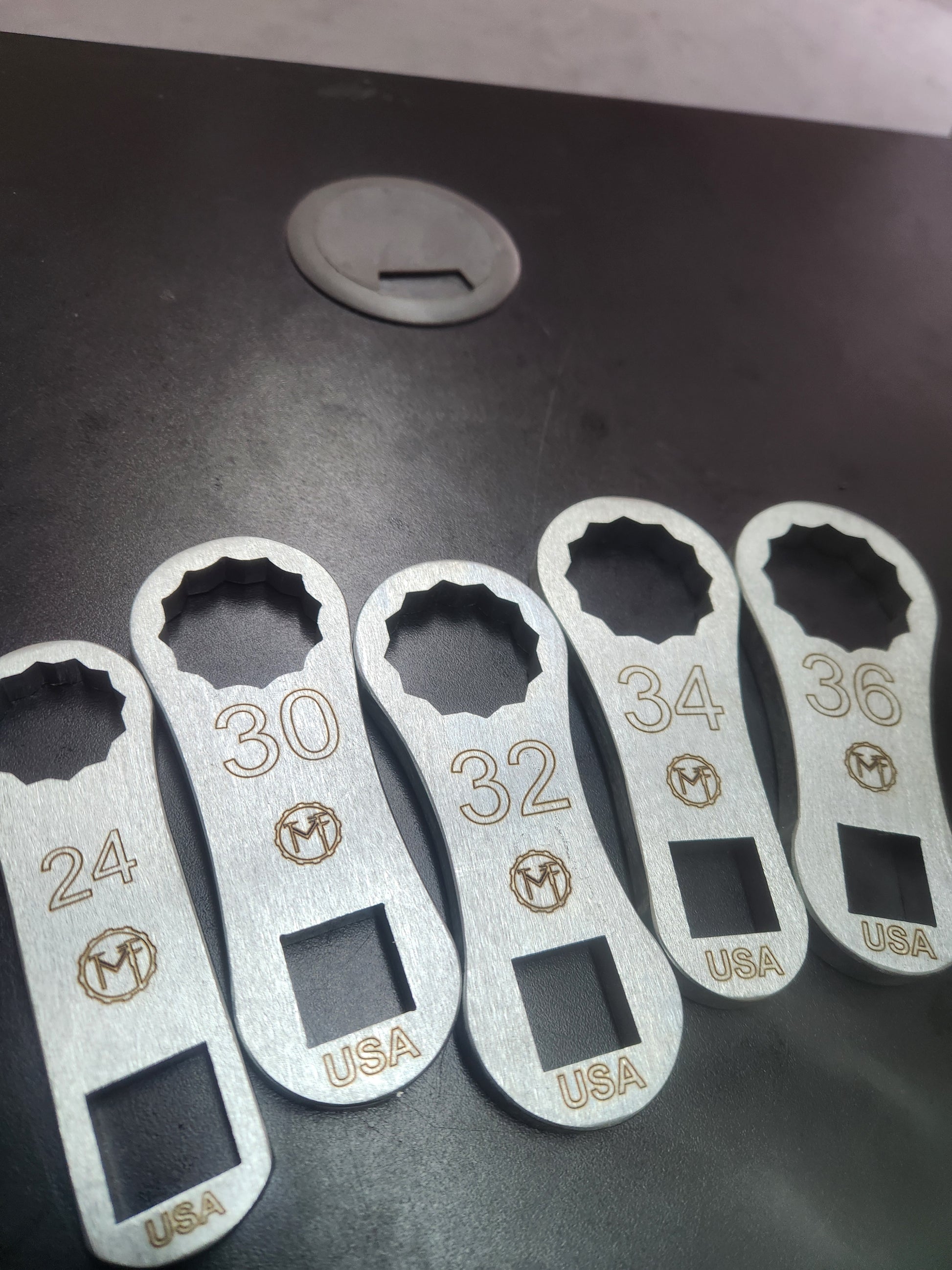 A set of metal dog bone-shaped wrenches in sizes 24mm, 30mm, 32mm, 34mm, and 36mm, with an electroplated coating and customizable etching offered. 