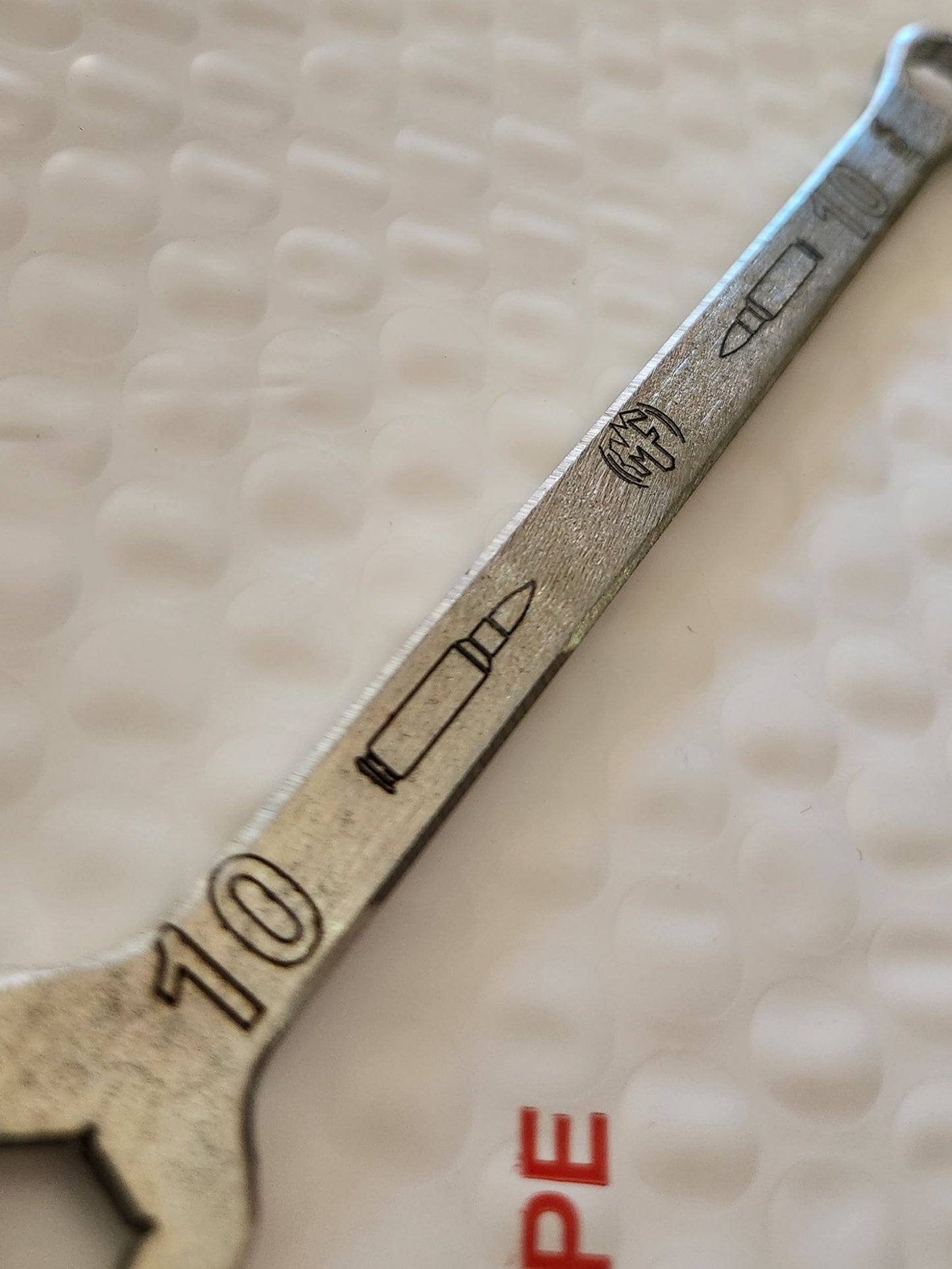 A silver 10mm combination wrench with laser engraved markings and an offset angle.